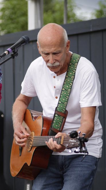 An elderly man intensely playing an acoustic guitar outdoors.