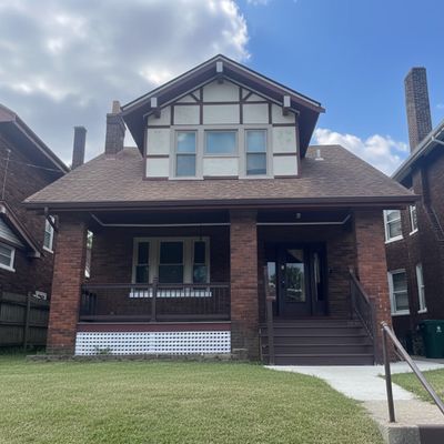 Brick house with a front porch and a gabled roof under a partly cloudy sky.