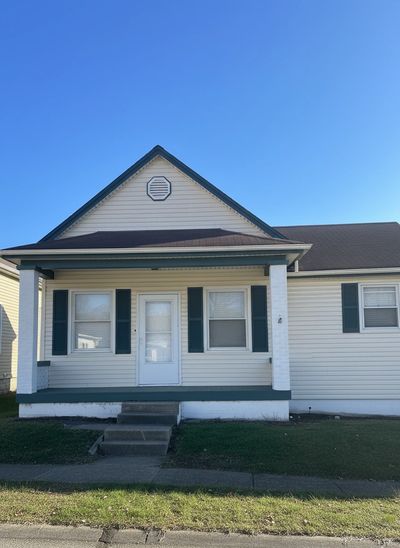 A small white house with green shutters and a front porch under a clear blue sky.