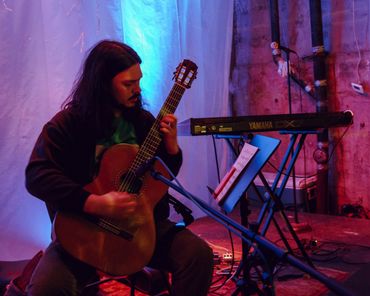 Man playing classical guitar on stage with colorful lighting.