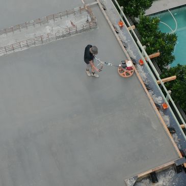 Worker smoothing freshly poured concrete on a rooftop near a pool.