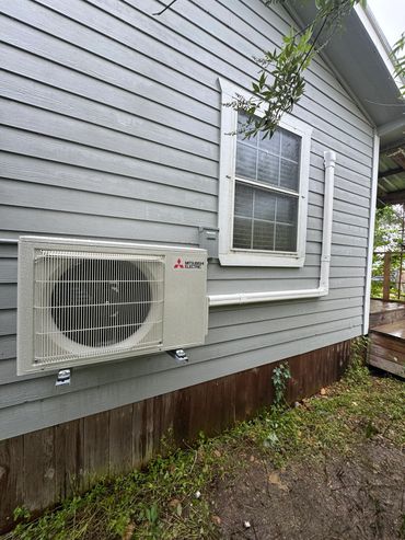 Mitsubishi Electric air conditioning unit mounted outside a gray wooden house.