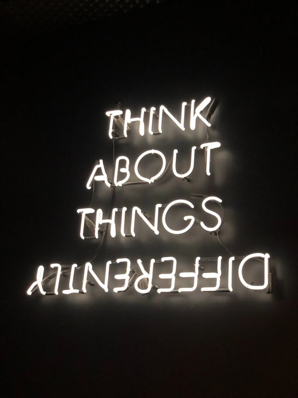 Neon sign reads 'THINK ABOUT THINGS DIFFERENTLY' with 'DIFFERENTLY' upside down.