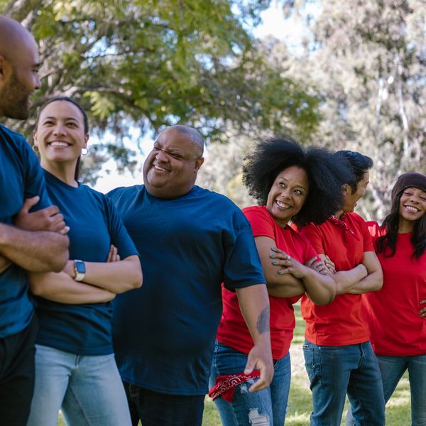 A diverse group of people in red and blue shirts smiling and chatting outdoors.