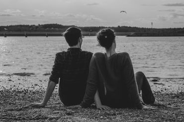 Two people engaged in conversation while sitting on the beach, captured in black and white
