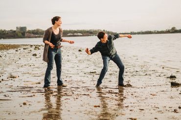 Two people playfully throwing stones by the waterside on a beach at dusk.