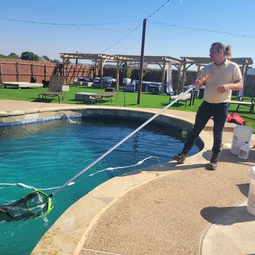 Pool boy, JD, cleaning a pool by skimming the water with a net on a pole.
