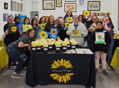 Group of people proudly displaying sunflower paintings at a community event.