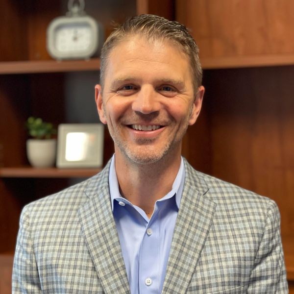 Smiling man in a checkered blazer and blue shirt.