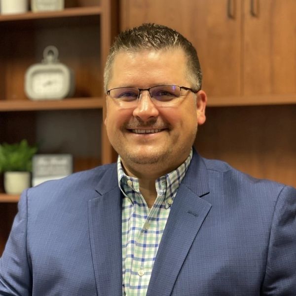 Smiling man in glasses and blue blazer in an office setting.