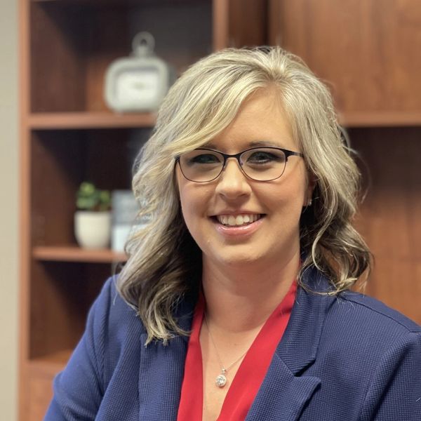 Professional woman smiling, wearing glasses and a blue blazer with a red blouse.