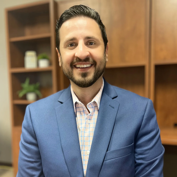 Smiling man in blue blazer posing in an office setting.