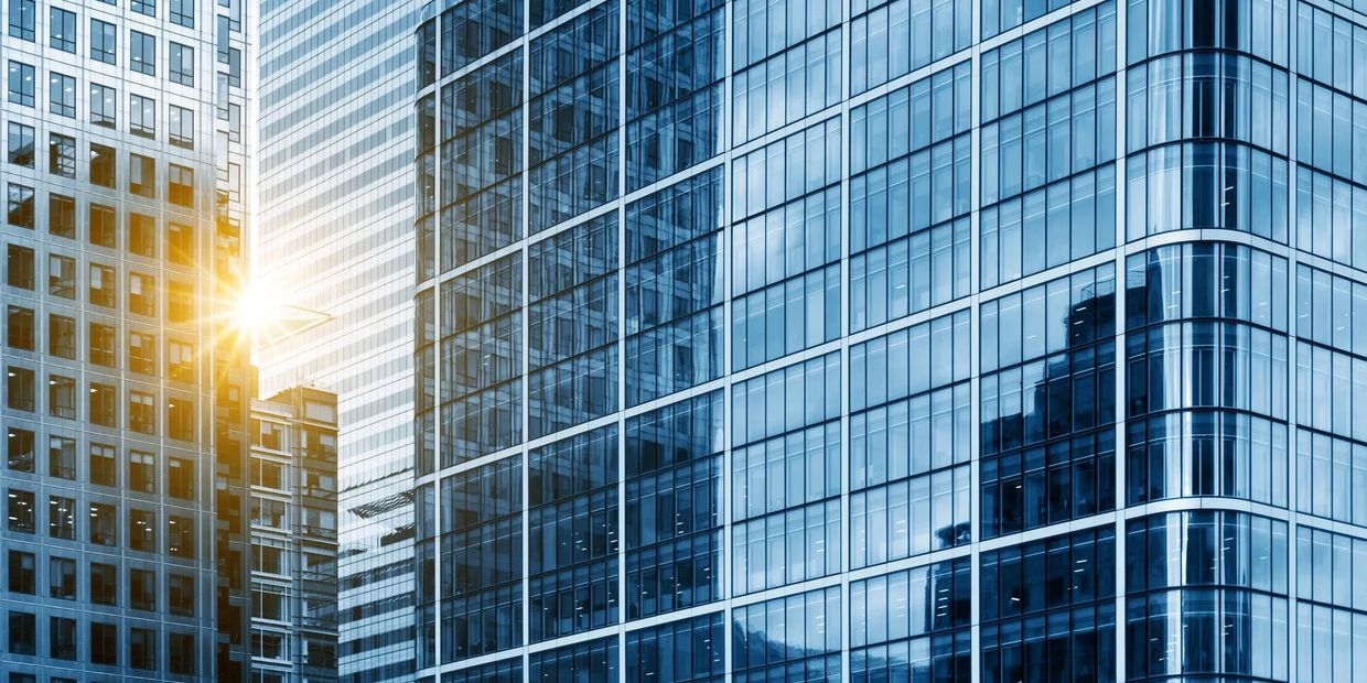 Sunlight shines between tall glass skyscrapers in a city.