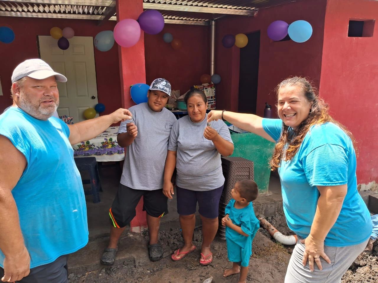 Two adults hand over keys to a couple standing outside a decorated home.