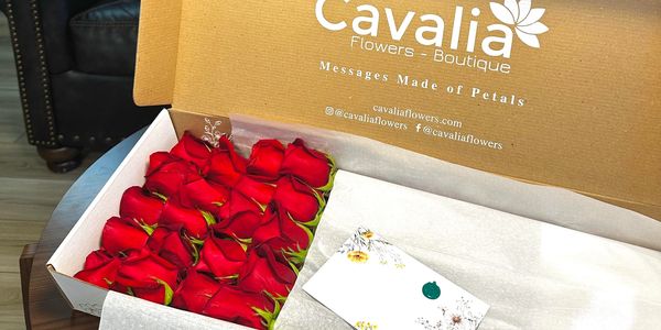 A box of red roses from Cavalia Flowers Boutique on a table in a living room.