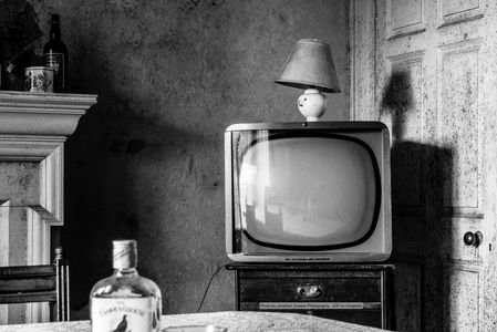 black and white photo of old tv blocking door and liquor bottle on table