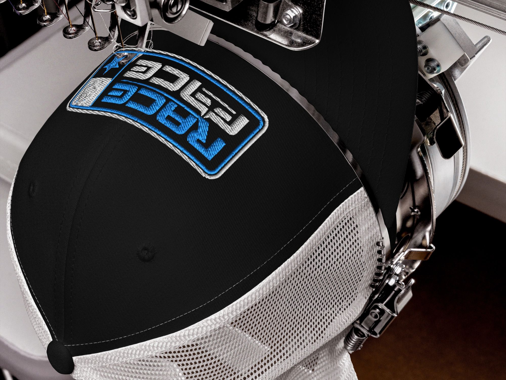 Embroidery machine stitching a blue and white logo on a black mesh cap.