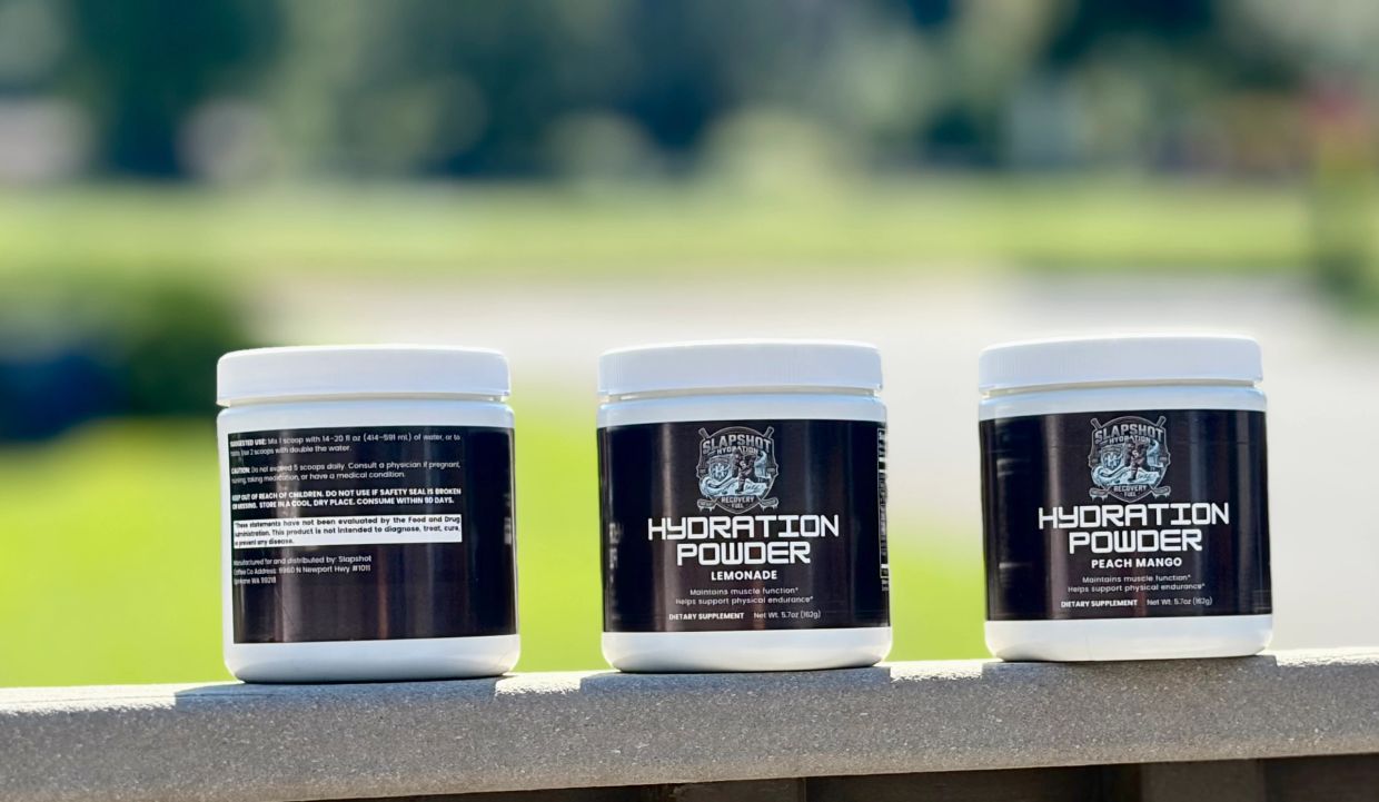 Three containers of Slapshot Hydration Powder on a ledge outdoors.