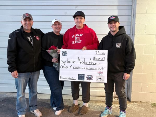 Four people holding a large check and flowers outdoors.