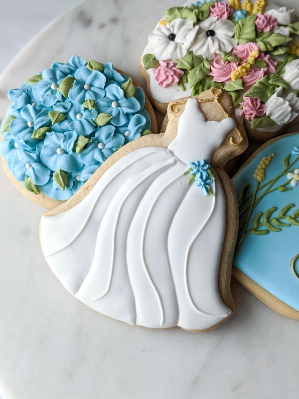 A sugar cookie shaped like a wedding gown in front of floral cookies