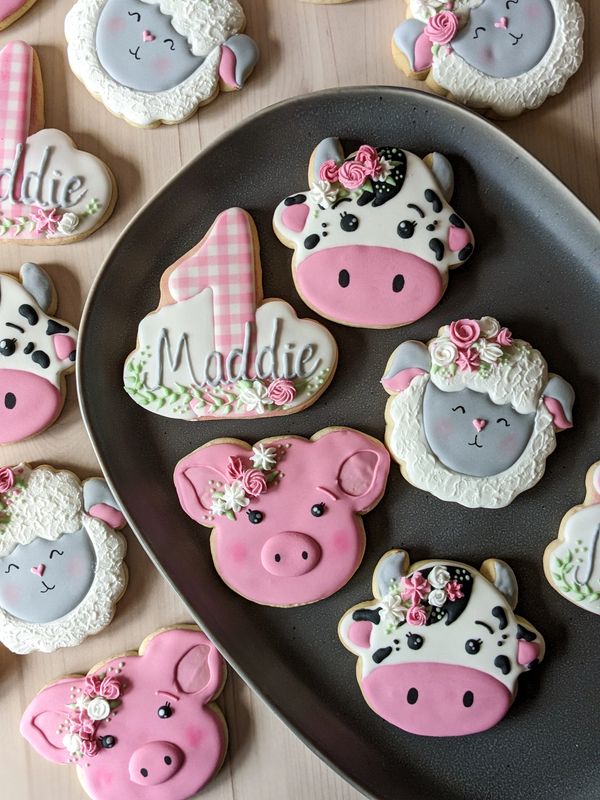 Cow, sheep, pig, and number one sugar cookies on a dark platter surrounded by more cookies