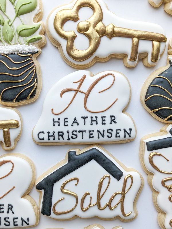 Realtor sugar cookies, including a "sold" house, a key, a house plant, and a logo sugar cookie