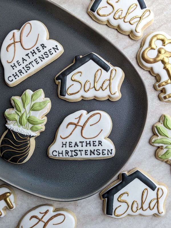 Realtor logo sugar cookies including a sold sign, a logo, a houseplant, and a key on a plate