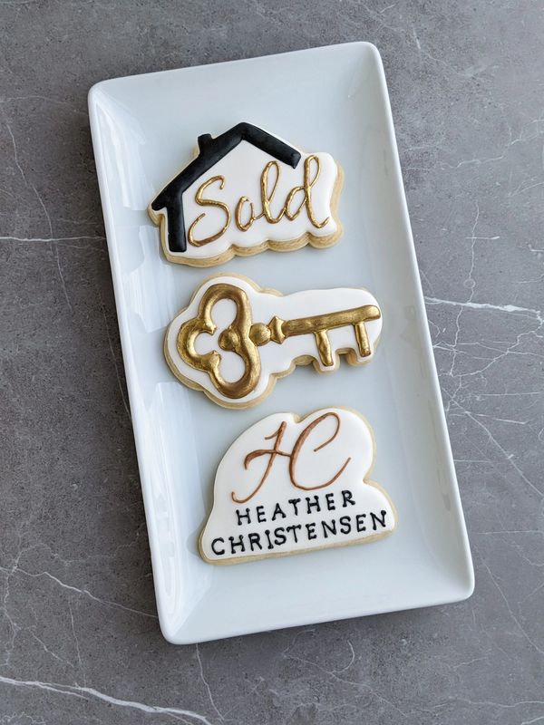 Realtor sugar cookies with a sold sign cookie, a key cookie, and a realtor logo cookie on a plate