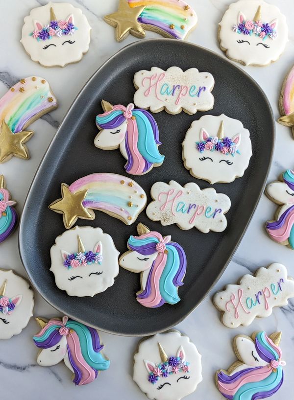 Unicorn sugar cookies arranged on a dark platter, with other sugar cookies around the plate