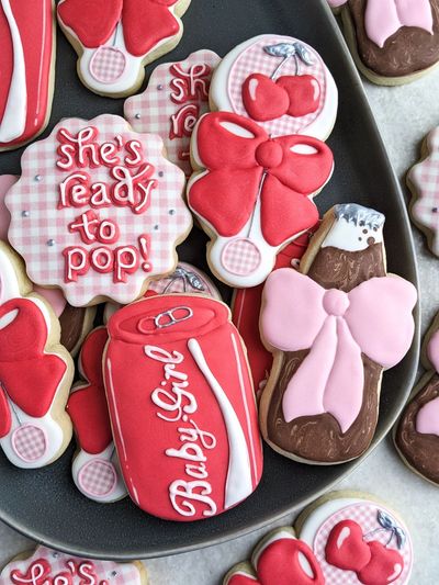 Sugar cookies themed, "She's About To Pop" with a baby rattle with cherry, soda bottle, cola can,