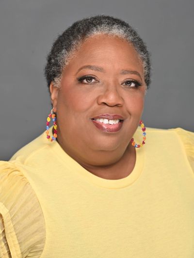 Smiling woman wearing colorful earrings and a yellow top.