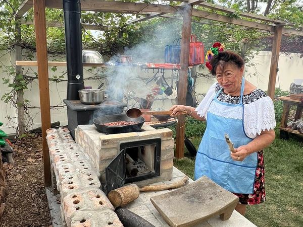 Woman cooking over a rustic outdoor stove, smiling warmly.
