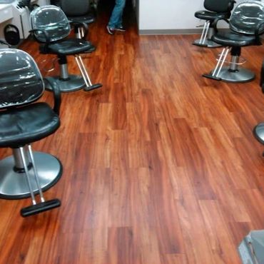 Empty black salon chairs with plastic covers on polished wooden floor.