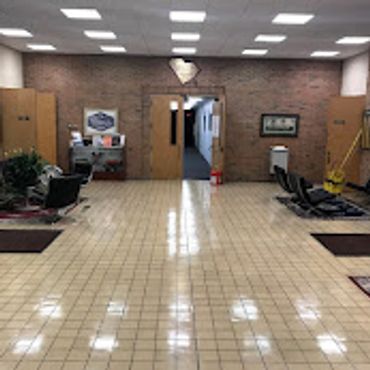 A spacious, tiled lobby with chairs and rugs along the walls.