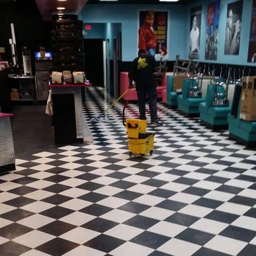 Person mopping the black-and-white checkered floor in a retro diner.