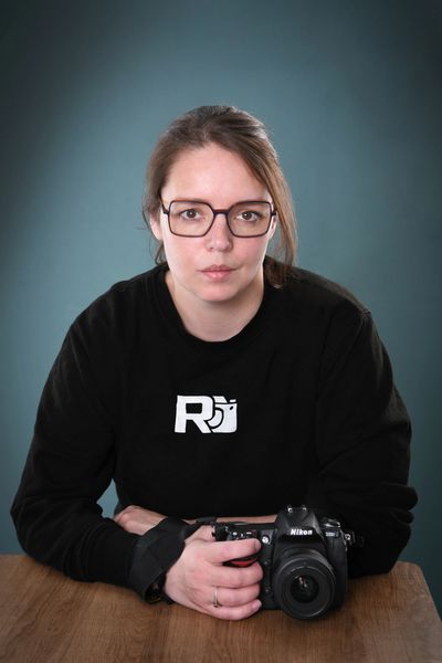 Woman with glasses holding a Nikon camera at a table.