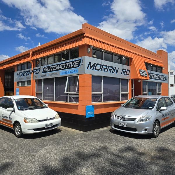 Automotive repair shop with two branded cars parked outside under a partly cloudy sky.
