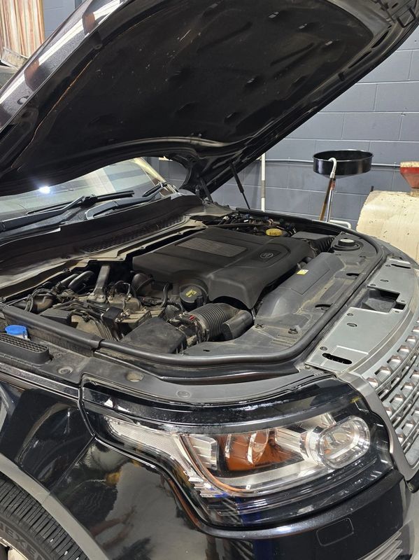 Black car with its hood open showing the engine in a garage.