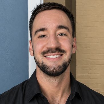 Smiling young man with short dark hair and a beard, wearing a black shirt.