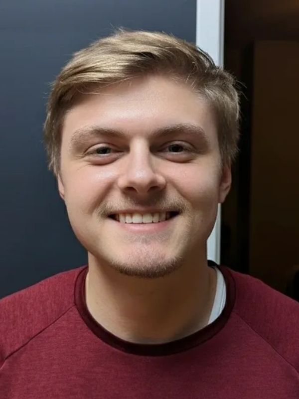 Smiling young man with light brown hair and a maroon shirt.