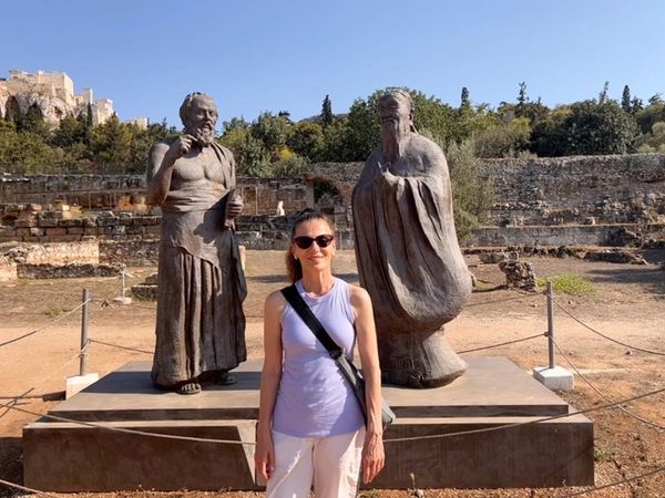 a woman standing between two large bronze statues of philosophers