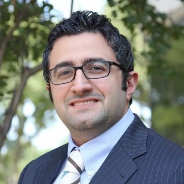 Man in glasses and suit smiling outdoors.