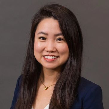Professional portrait of a smiling woman with long dark hair and a navy blazer.