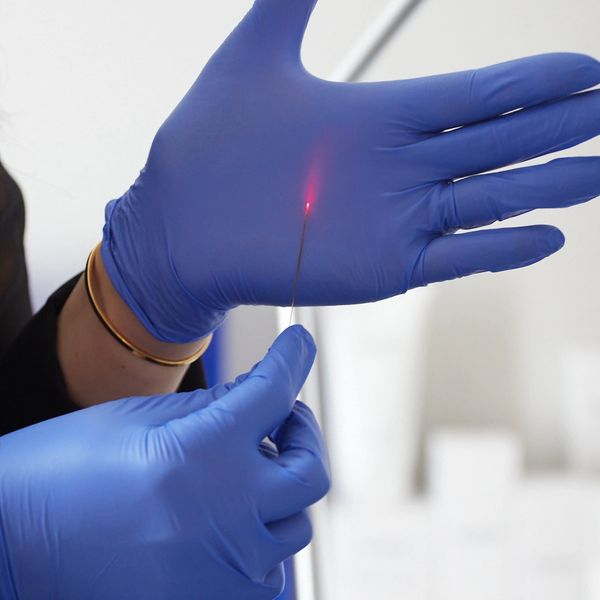 Gloved hands holding a needle with a glowing red tip, possibly for laser therapy. Endolift