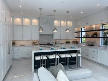 Modern white kitchen with marble countertops and pendant lights.