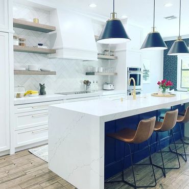 Modern kitchen with white marble island and blue base, brown stools, and black pendant lights.