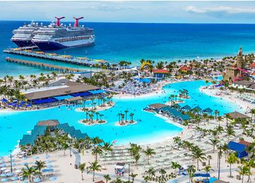 A large cruise ship docked near a tropical resort with pools and palm trees.