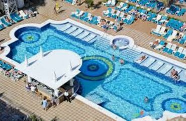 A vibrant outdoor swimming pool with sun loungers and people relaxing.