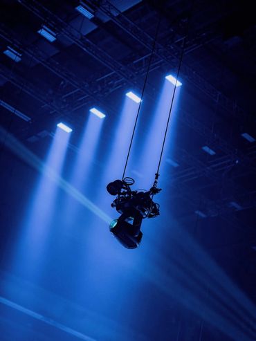 A camera suspended by cables under blue stage lights.