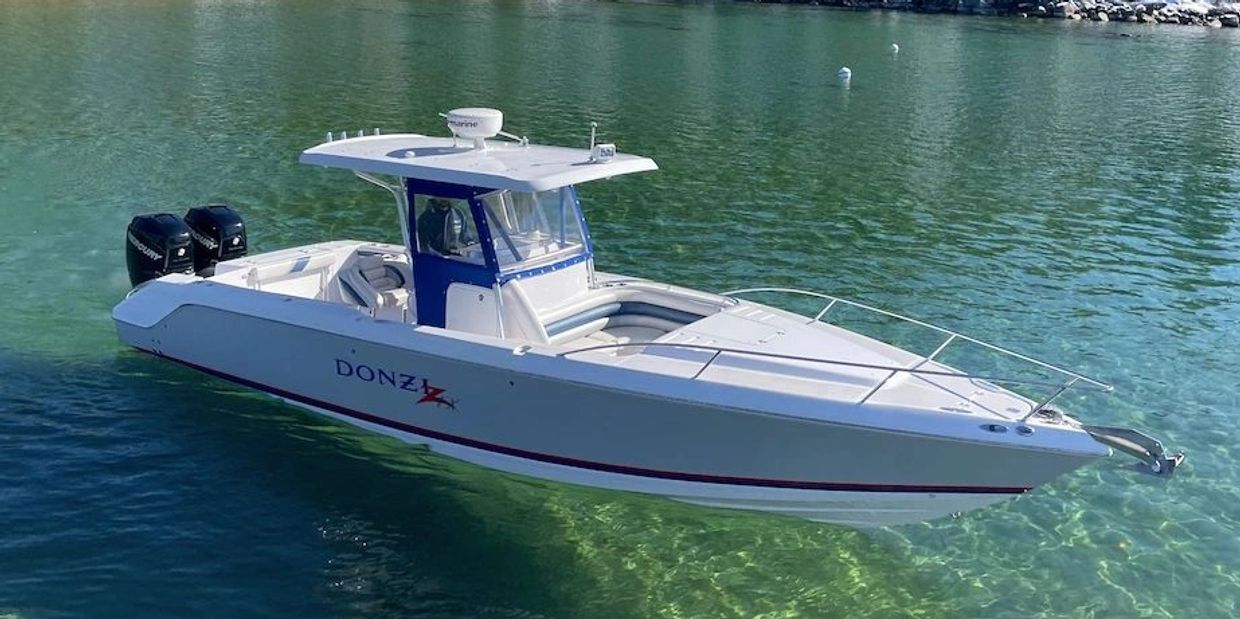 White Donzi powerboat floating on clear greenish water near shore.